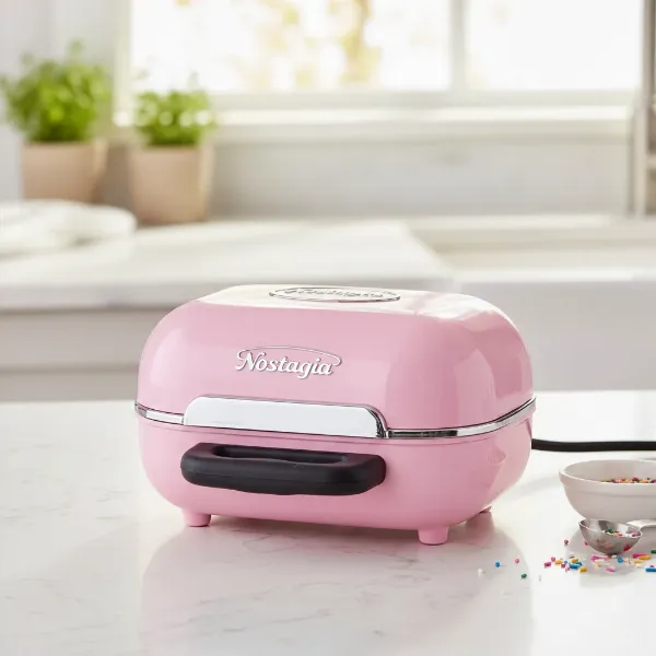 Compact pink Nostalgia MyMini Cupcake Maker on a clean kitchen counter, ready for use.